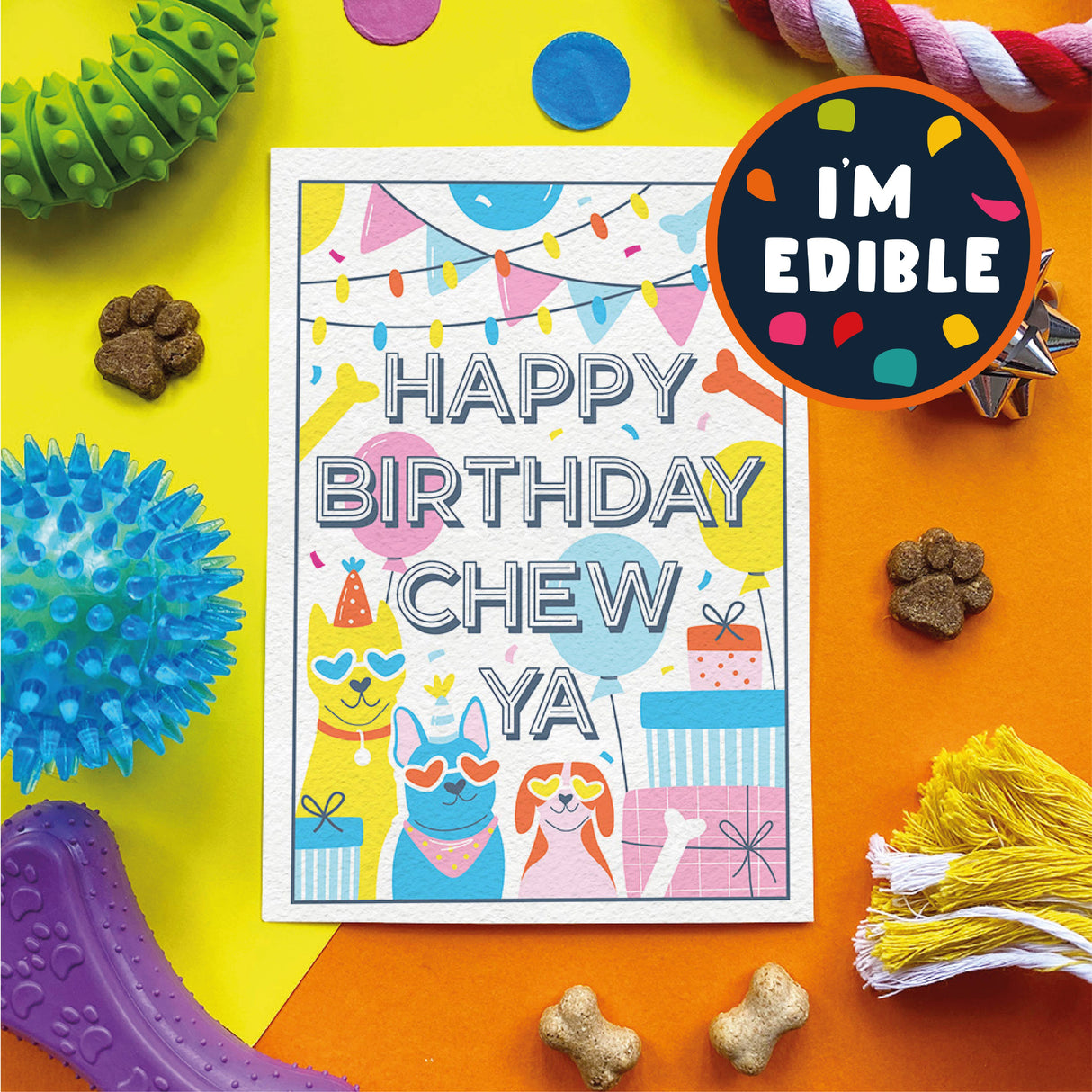 A colorful pet birthday card reading 'HAPPY BIRTHDAY CHEW YA' is displayed on a bright yellow and orange background with dog treats, dog toys, and a circular badge that says 'I'M EDIBLE'.
