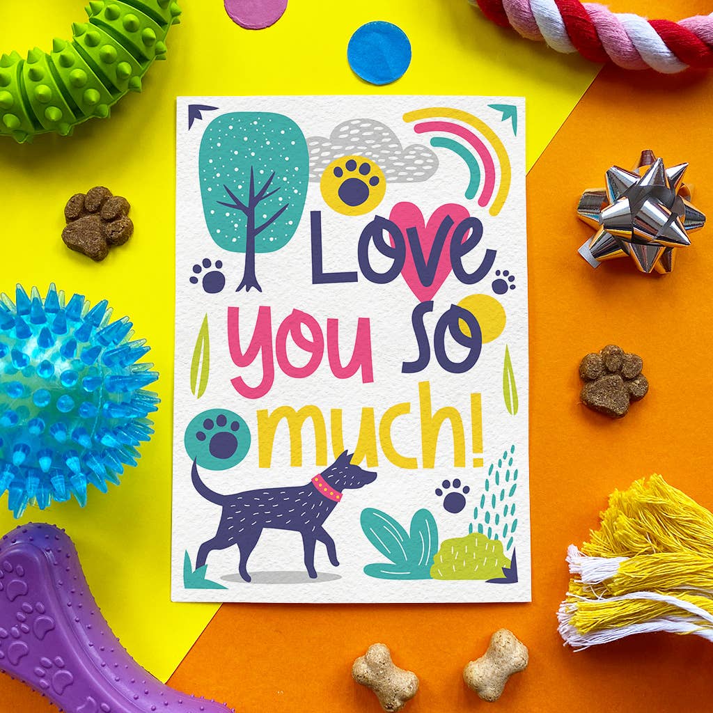 A square greeting card with a colorful 'Love you so much!' design featuring a dog, paw prints, and playful illustrations, styled in a flat-lay with dog toys and treats on a bright yellow and orange background.